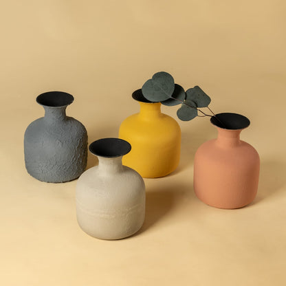 A group of four textured vases in grey yellow beige and peach tones arranged together on a warm background showcasing their shapes and earthy finish.