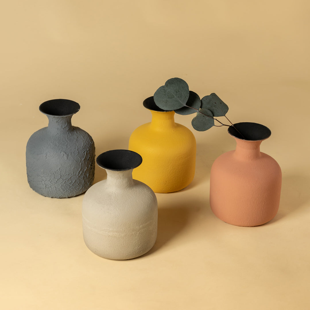 Collection of four colorful matte metal vases with greenery for vibrant modern home decor and artistic table styling.