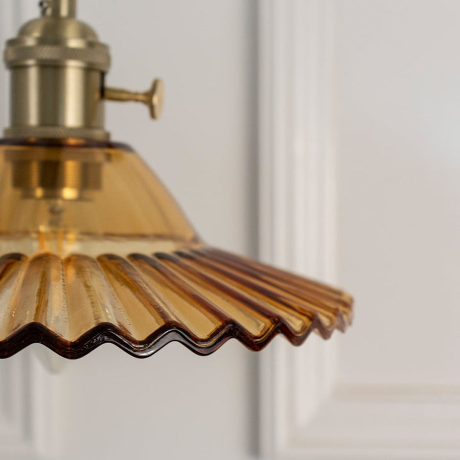 Closeup of amber ruffle glass pendant lamp showing detailed scalloped rim and golden holder with twisted cord.
