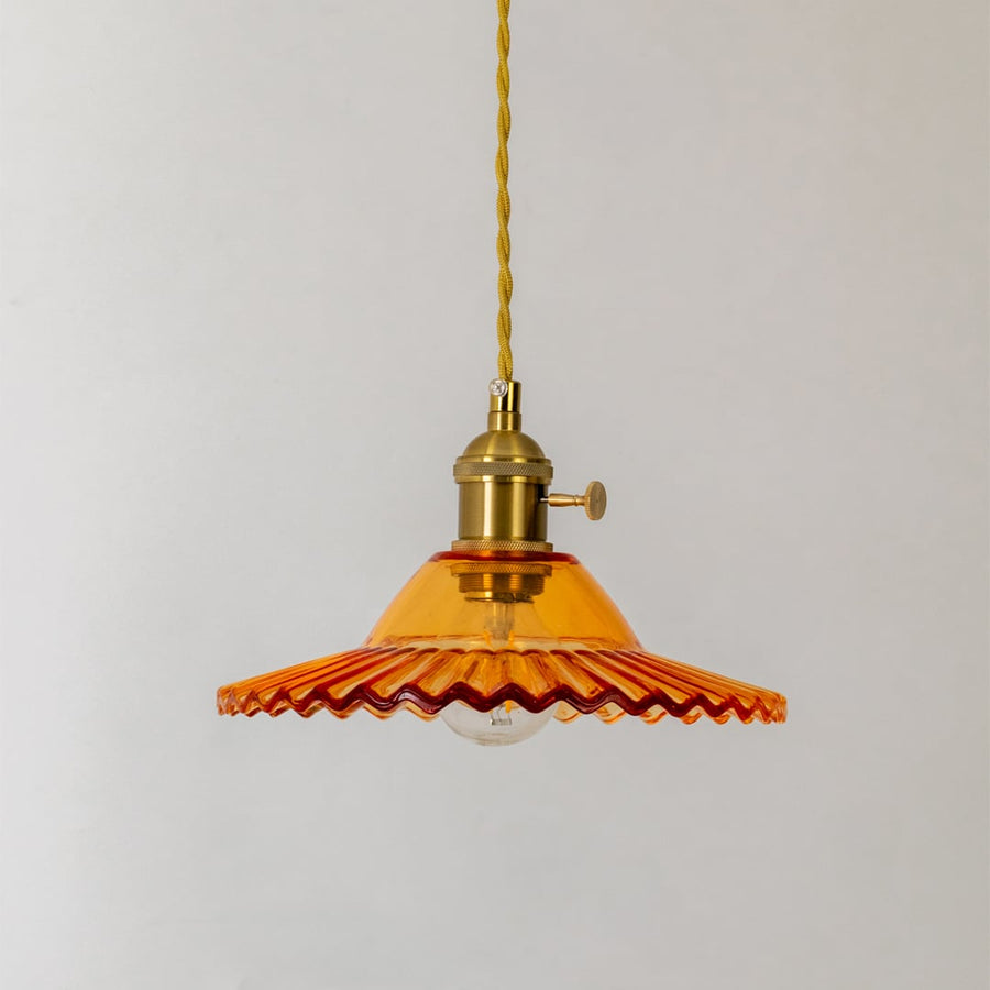 Amber ruffle glass pendant light turned off with scalloped edges and antique brass holder displayed on a white background.