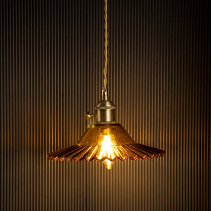 Amber ruffle glass pendant lamp illuminated beautifully against a black ribbed background highlighting its fluted design.