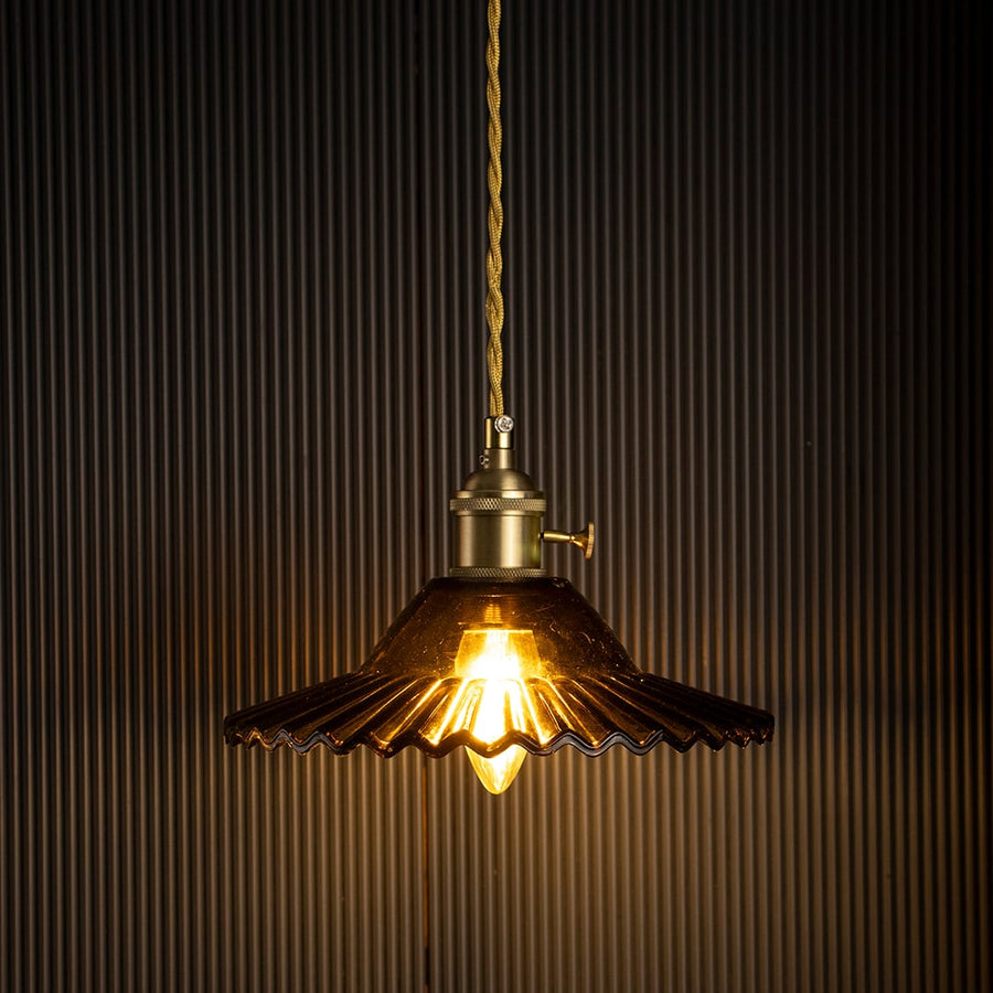 Glowing vintage pendant light against black background with ribbed amber glass shade highlighting timeless craftsmanship and warm lighting.