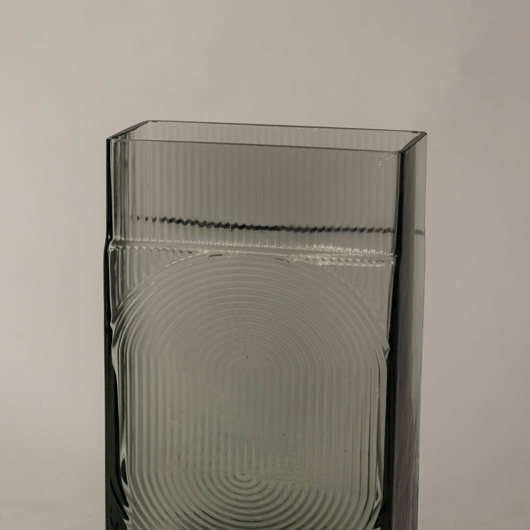 Closeup of textured smoky gray glass vase showcasing fine ribbed surface and geometric circular detailing.