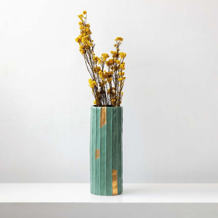 Yellow dried statice flower stems styled in tall green ceramic vase with gold accents against white background decor.