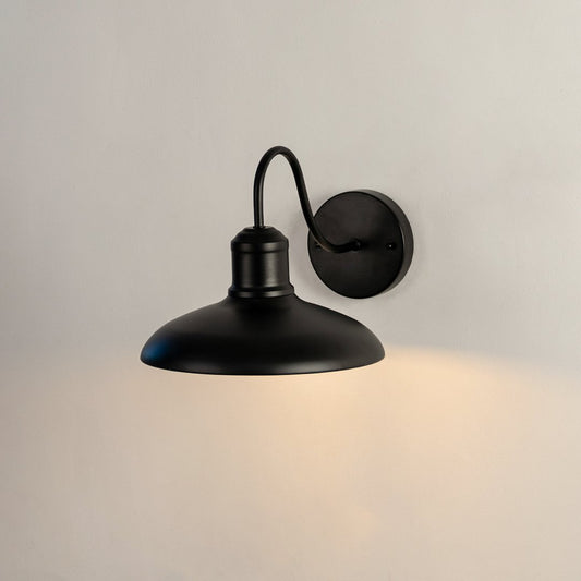 Matte black metal gooseneck barn light on white background casting warm downward illumination for outdoor patio decor.