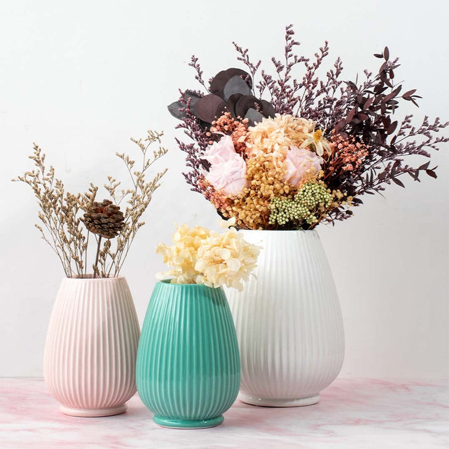 Set of three ribbed ceramic vases in white teal and pink shades each with unique floral arrangements for elegant tabletop styling.