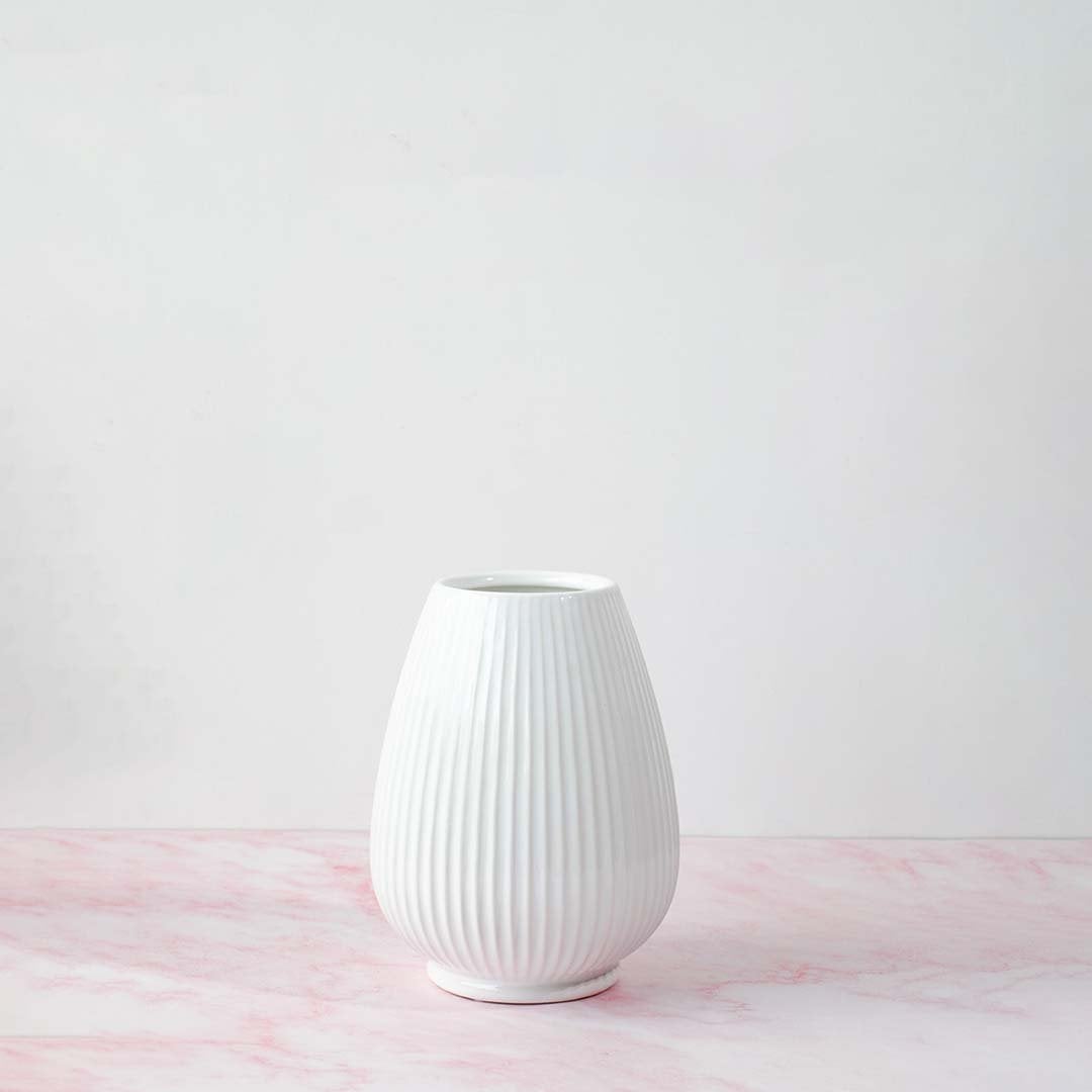 White ribbed ceramic vase with natural lighting on white background creating a soft shadow and minimalist artistic vibe.