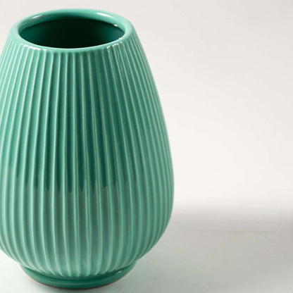 Closeup of ribbed green ceramic vase showing smooth glossy texture and elegant modern round shape.