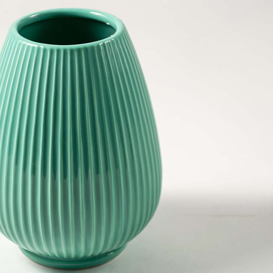 Closeup of ribbed green ceramic vase showing smooth glossy texture and elegant modern round shape.