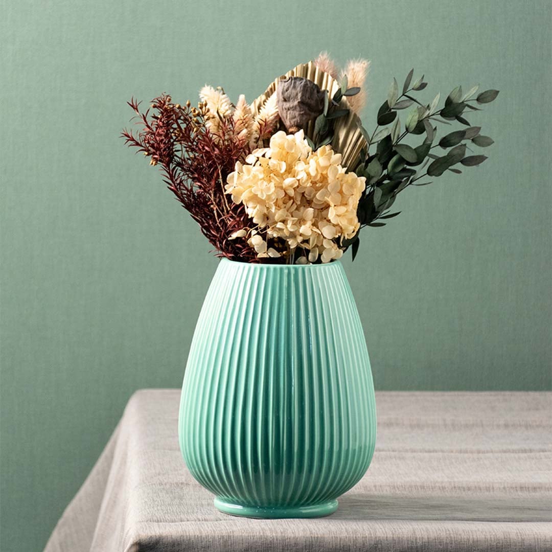 Stylish green ceramic vase with dried flowers placed on table for modern living room and dining decor.