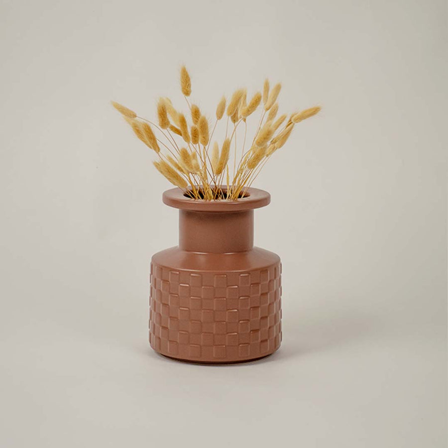 Brown ceramic vase with geometric texture styled beside dried flowers brings organic charm to living room decor.