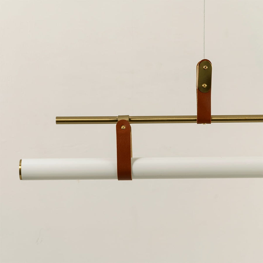 Closeup of gold linear pendant light showing white tubular diffuser leather strap accents and refined craftsmanship.