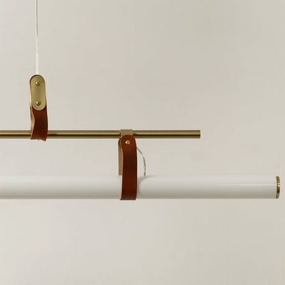 Detailed closeup of gold linear pendant light showing metallic frame leather straps and smooth white diffuser tube.