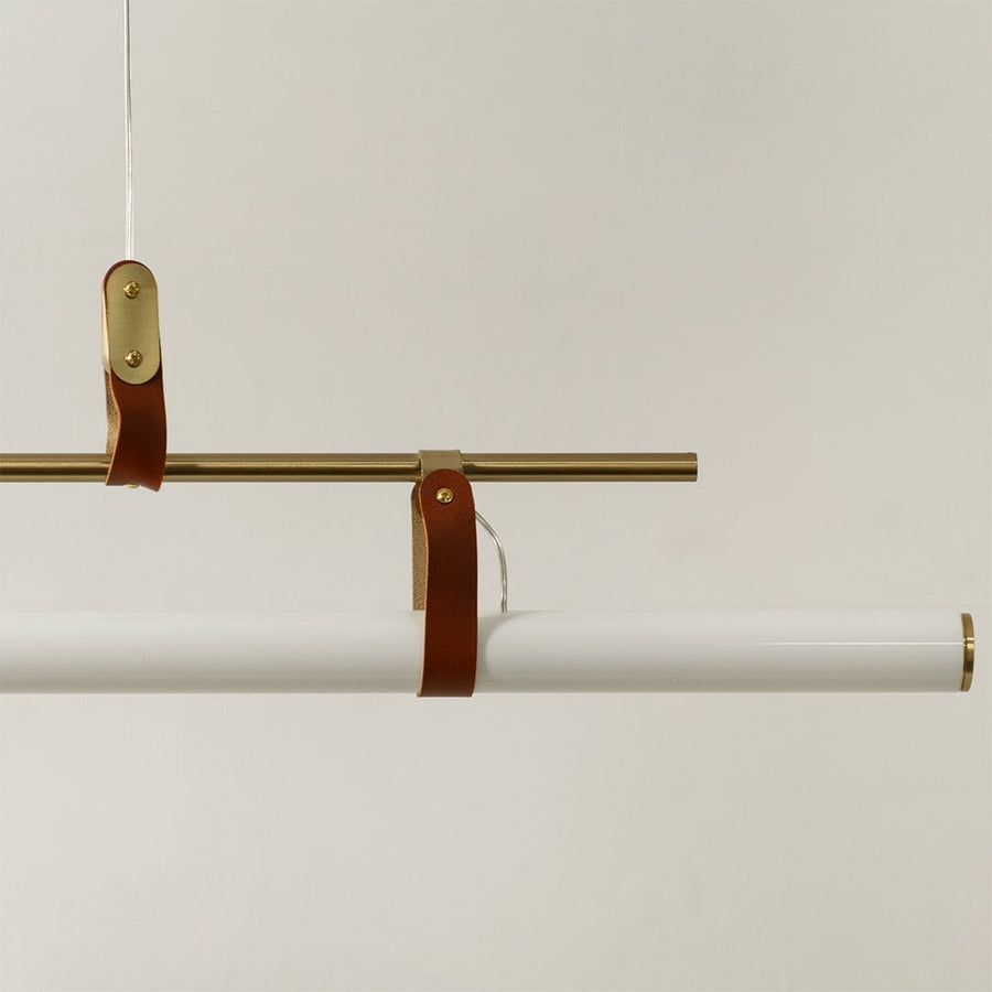 Detailed closeup of gold linear pendant light showing metallic frame leather straps and smooth white diffuser tube.