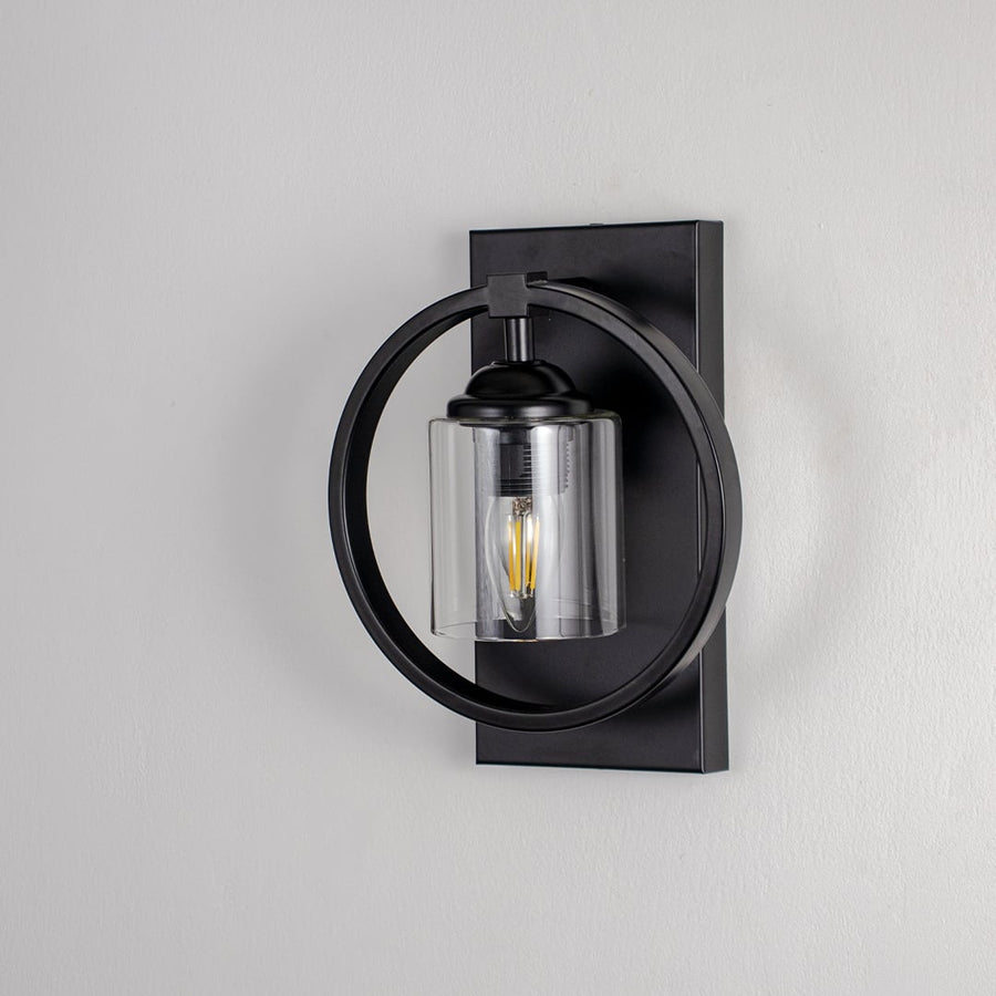 Black circular frame wall light with clear glass shade and exposed bulb shown off on white background for modern interiors.