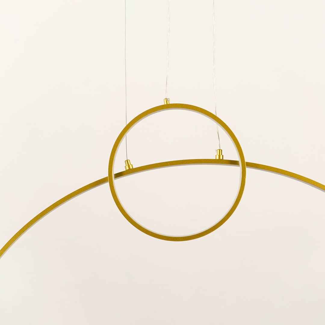 A modern gold ring ceiling light with a curved bar design ideal as a minimal LED chandelier for contemporary home interiors and designer lighting décor.