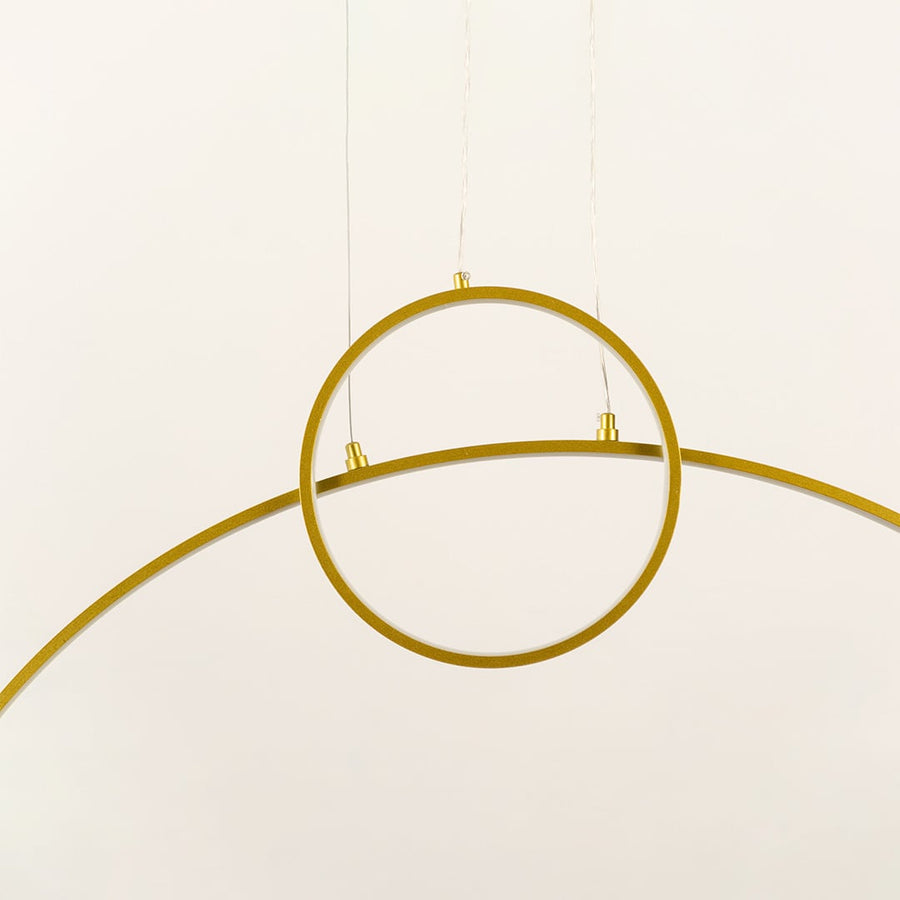 A modern gold ring ceiling light with a curved bar design ideal as a minimal LED chandelier for contemporary home interiors and designer lighting décor.
