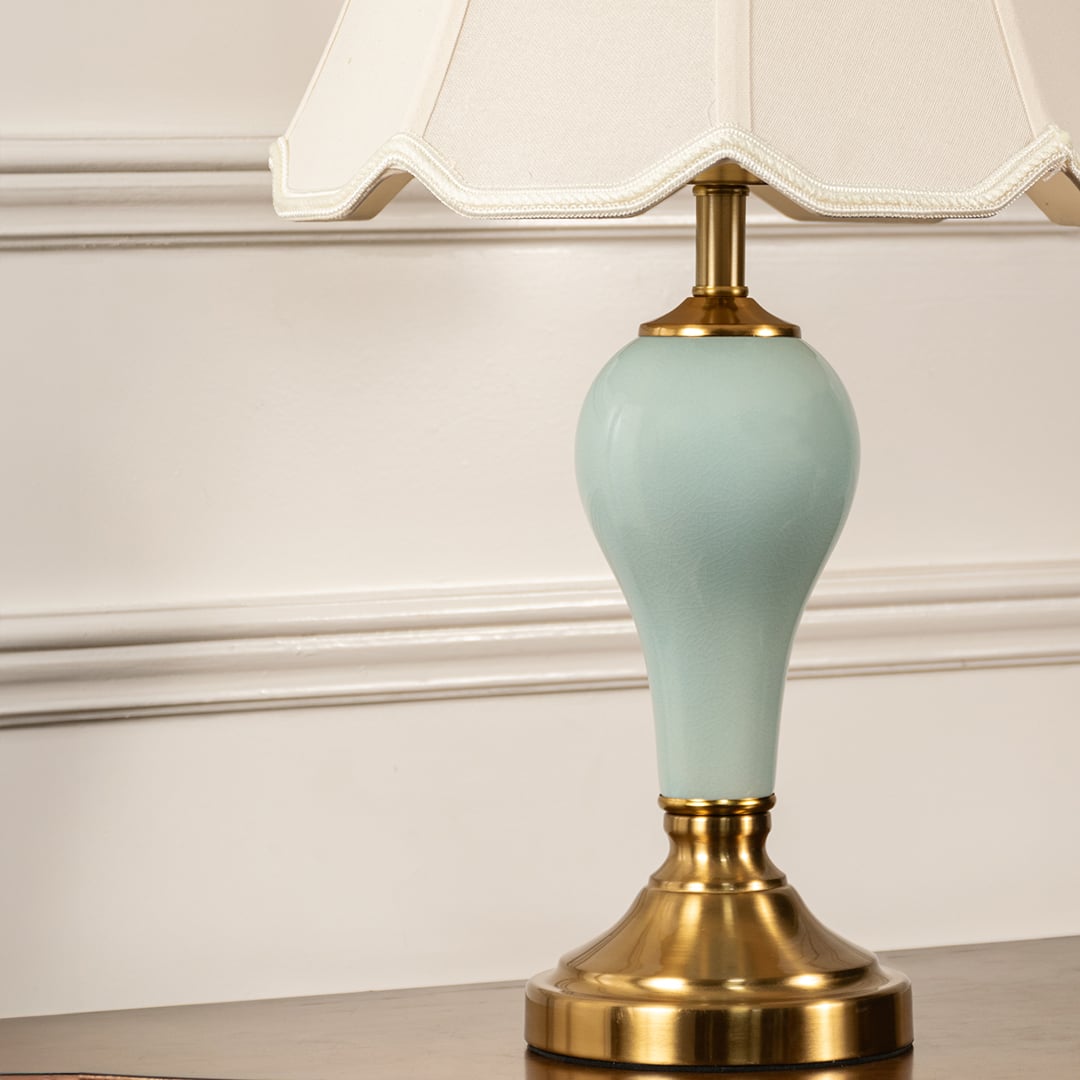 Close-up of table lamp showing detailed beige fabric shade trim and smooth blue ceramic body with golden base accent.