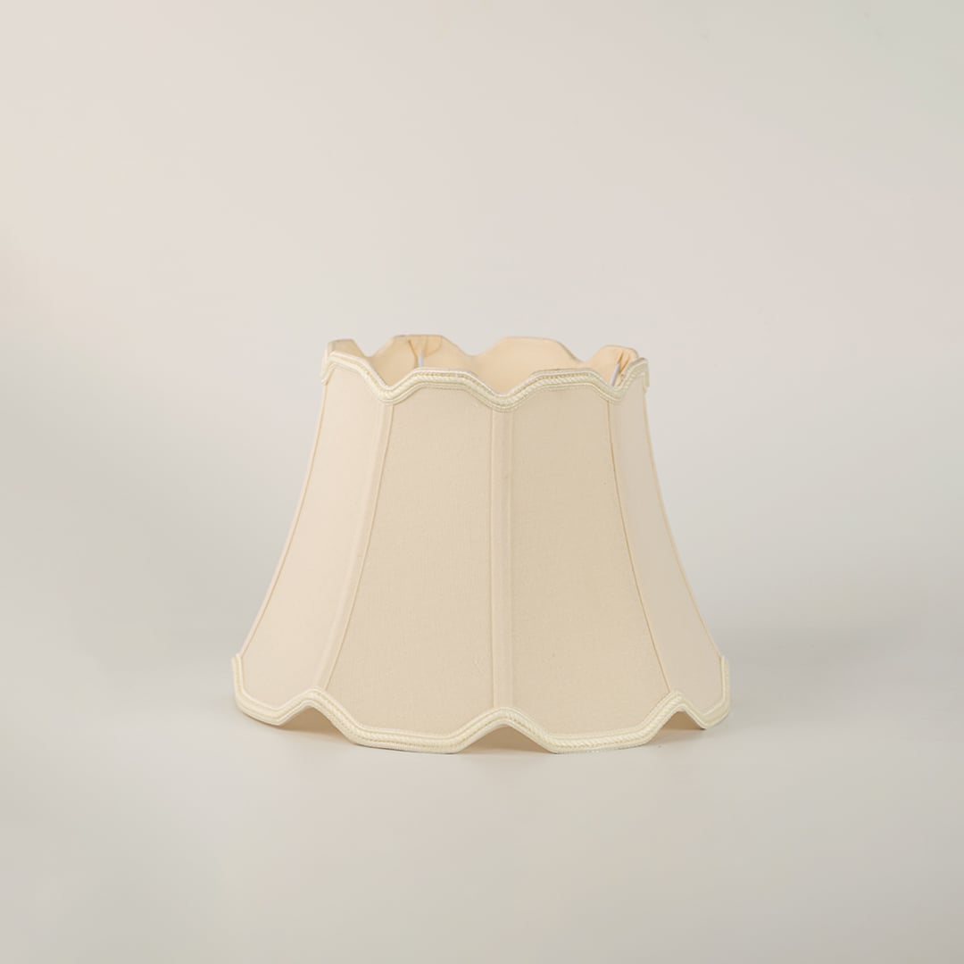 Beige scalloped fabric lamp shade with subtle trimming placed on a plain white background showcasing its elegant structure.