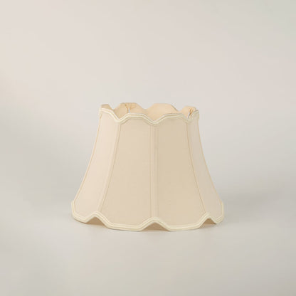 Beige scalloped fabric lamp shade with subtle trimming placed on a plain white background showcasing its elegant structure.