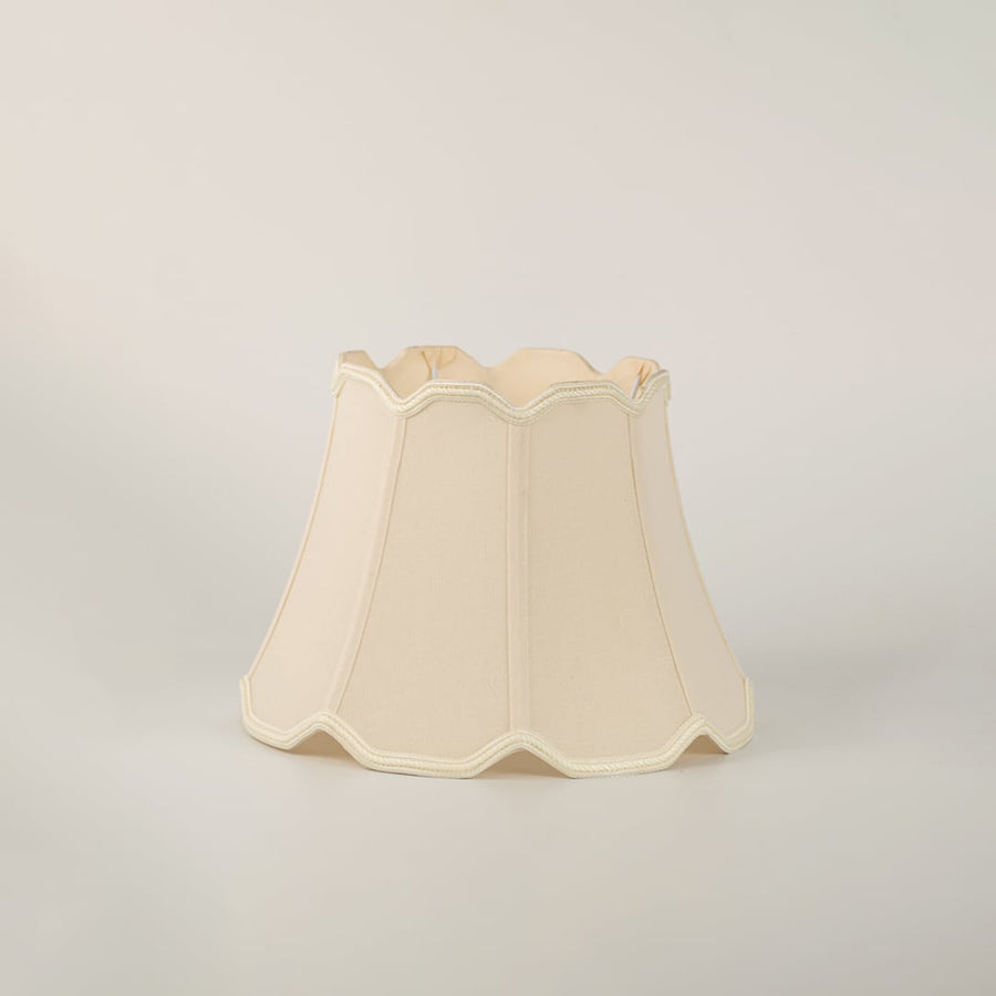 Beige scalloped fabric lamp shade with subtle trimming placed on a plain white background showcasing its elegant structure.