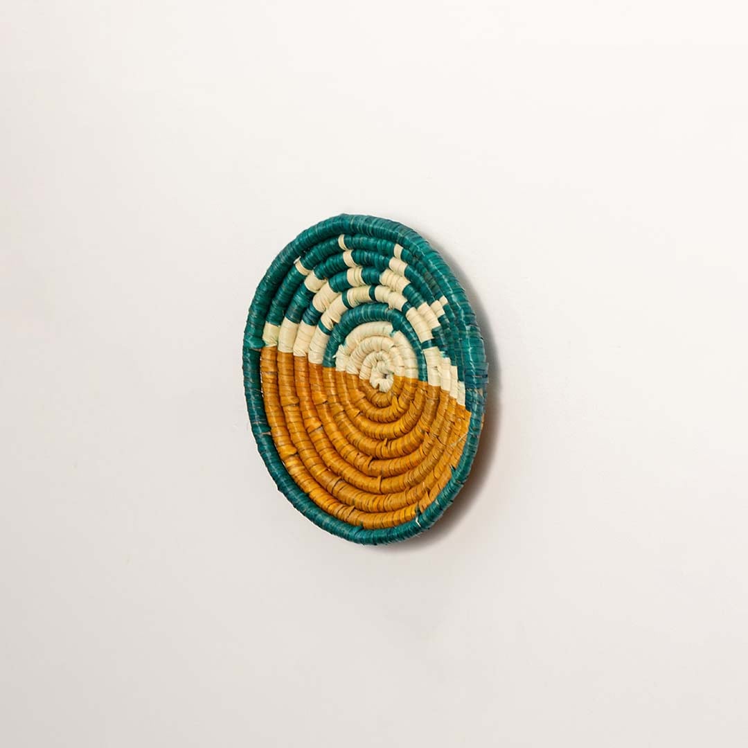 Side profile of the flat woven wall basket showing the thick natural fiber coils and teal wrapping details on a white surface for quality.