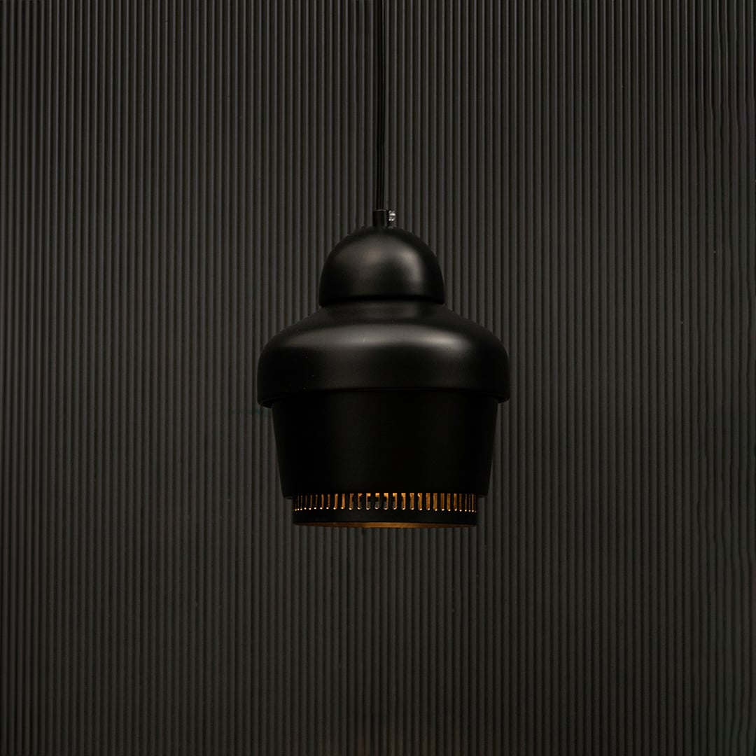 Black industrial pendant light with ribbed detailing against dark panel wall with light on for contemporary décor.