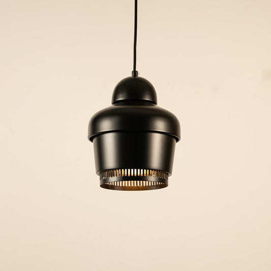 Black industrial pendant light with ribbed detailing hanging against plain background with light on for modern contemporary décor.