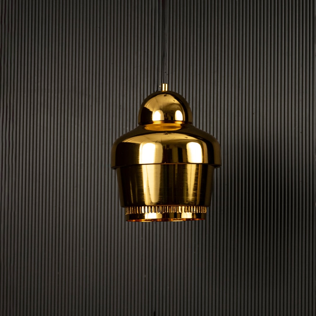 Gold industrial pendant light with ribbed detailing hanging against dark textured wall with light off for luxury modern décor.