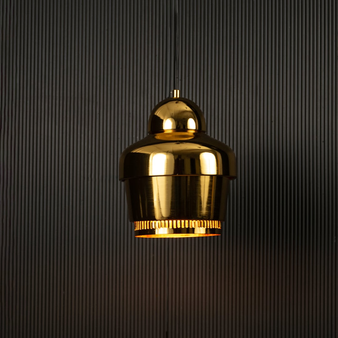 Gold industrial pendant light with ribbed detailing against dark panel wall with light on for luxury modern décor.