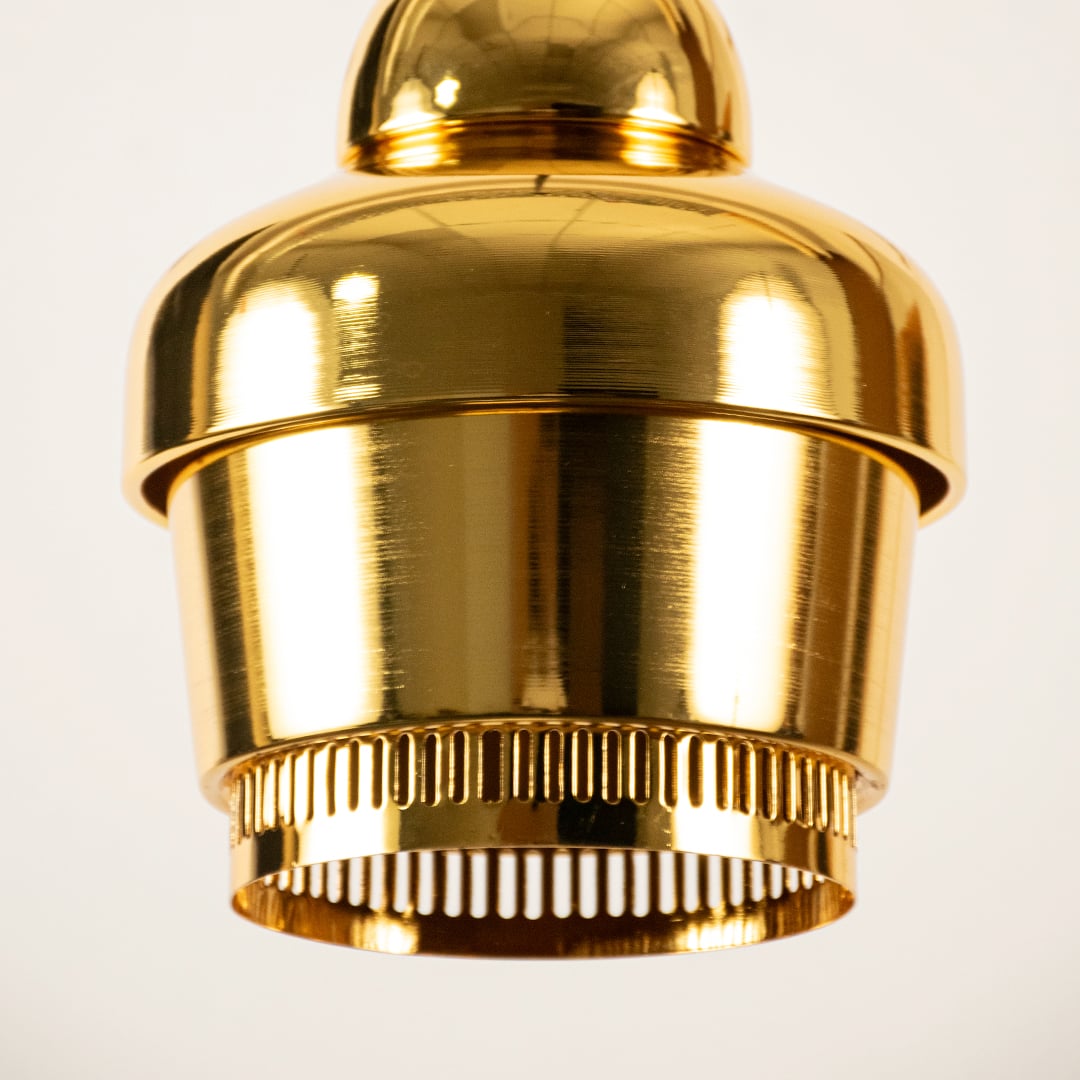 Gold industrial pendant light shown in close up view with ribbed detailing against plain background for luxury modern décor.