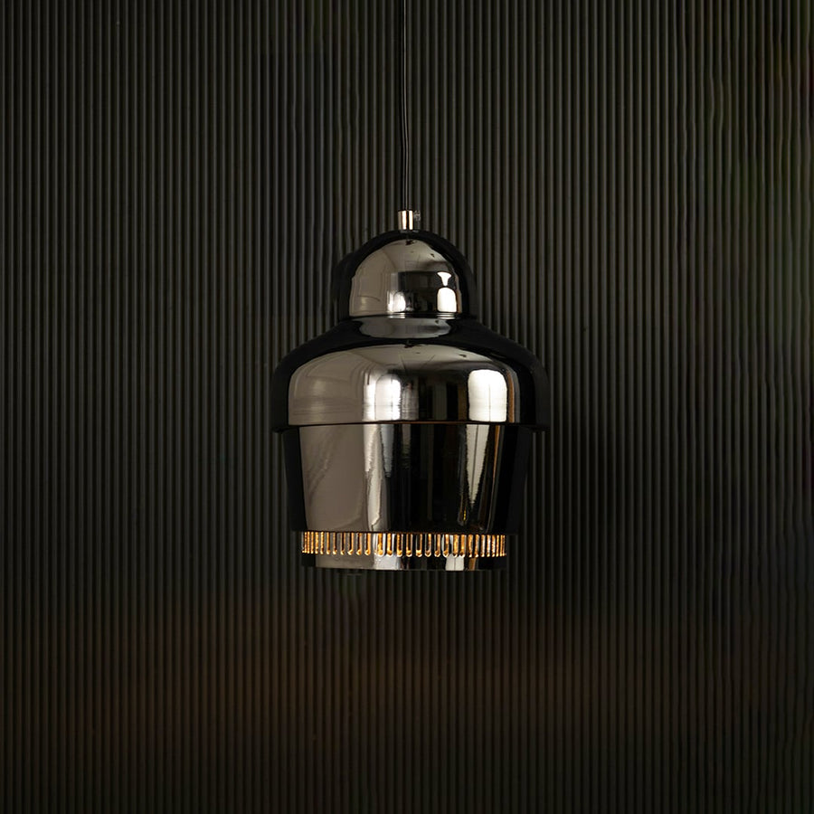 Chrome industrial pendant light with ribbed detailing against dark panel wall with light on for sleek modern décor.