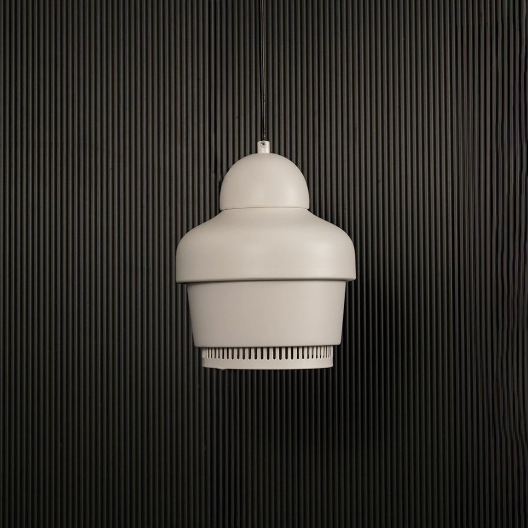 White industrial pendant light with ribbed detailing hanging against dark textured wall with light off for clean modern décor.