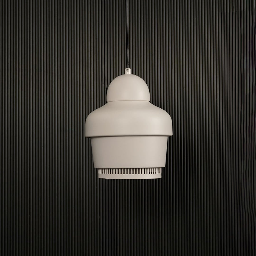 White industrial pendant light with ribbed detailing hanging against dark textured wall with light off for clean modern décor.
