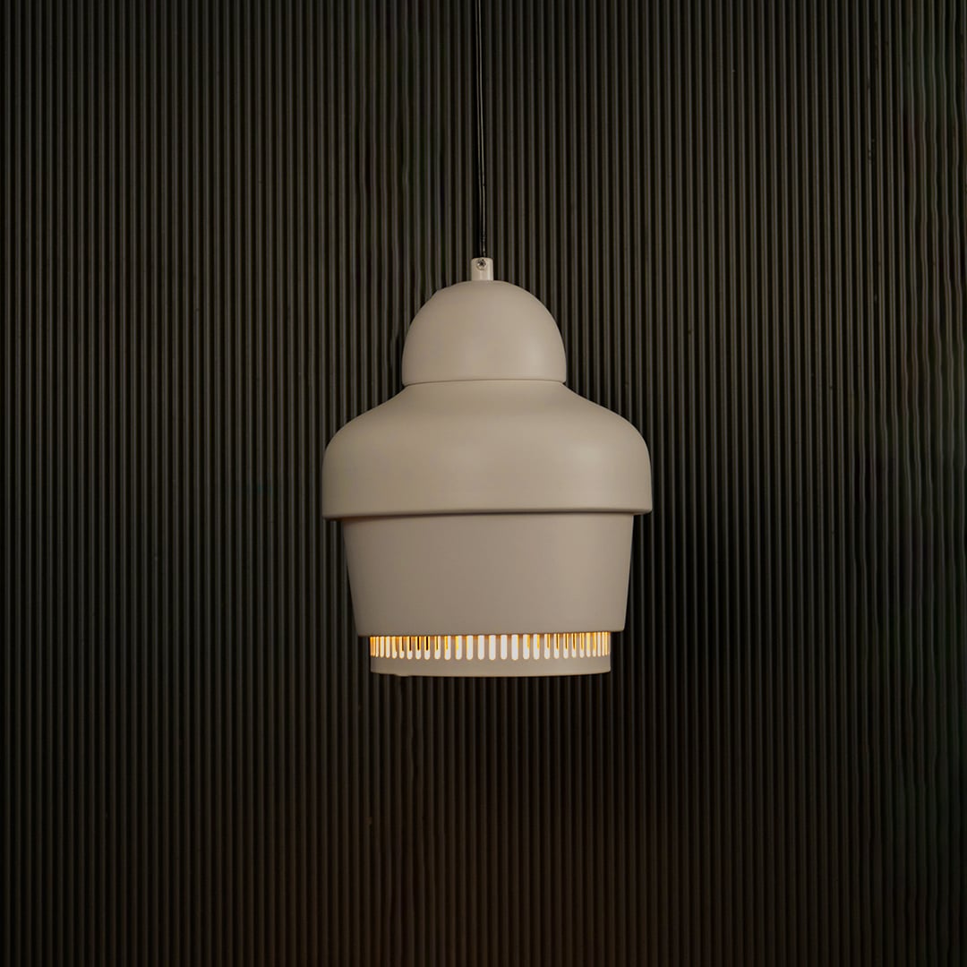 White industrial pendant light with ribbed detailing against dark textured wall with light on for clean minimal décor.