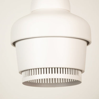 White industrial pendant light shown in close up view with ribbed detailing against plain background for clean minimal décor.