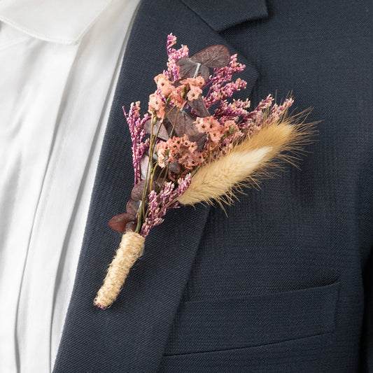 Closeup of boutonniere with pink dried flowers brown leaves and wheat grass wrapped in jute on suit lapel.
