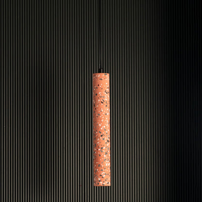 Terracotta cylinder pendant light turned off highlighting terrazzo design and cylindrical elegance against black background.