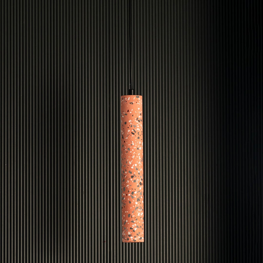 Terracotta cylinder pendant light turned off highlighting terrazzo design and cylindrical elegance against black background.