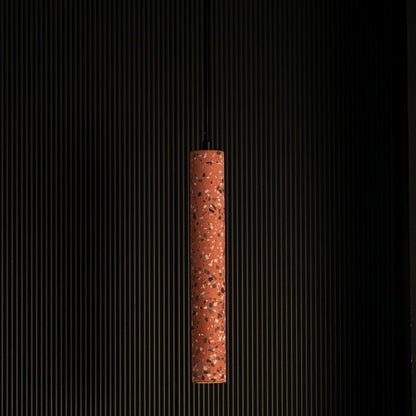 Terracotta cylinder pendant light turned on glowing warmly with terrazzo finish and brass detailing against dark background.