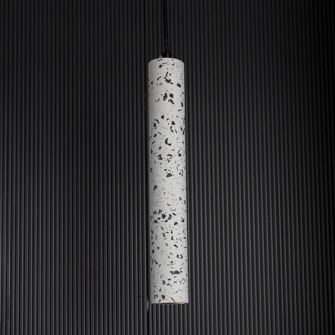 Terrazzo pendant light turned on against dark backdrop highlighting its speckled finish and refined minimalist design.