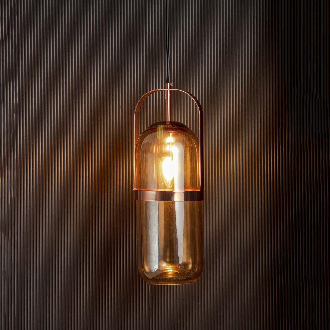 Amber glass pendant light glowing warmly with golden frame against black background creates cozy ambient decor.