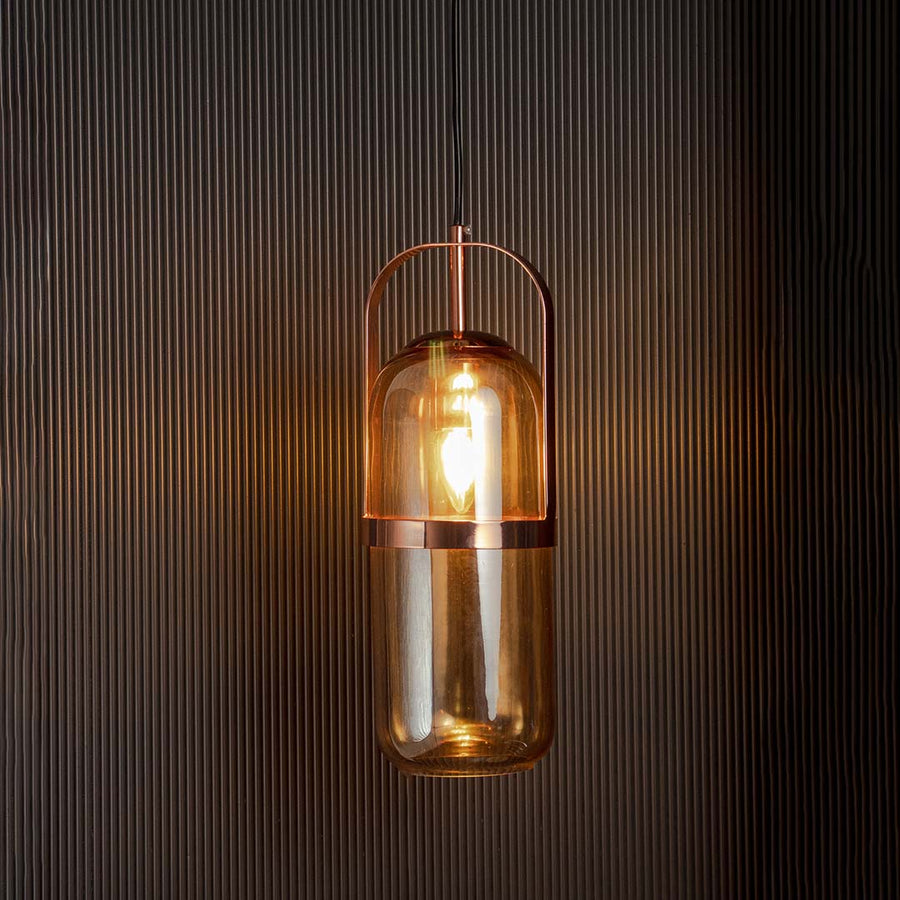 Amber glass pendant light glowing warmly with golden frame against black background creates cozy ambient decor.