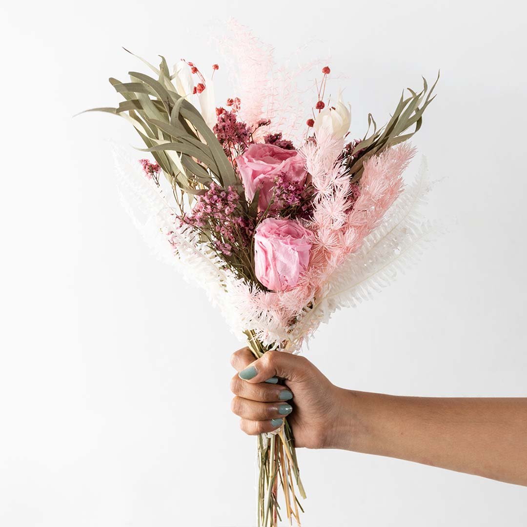 Hand holding a pastel pink rose dried bouquet mixed with green eucalyptus leaves and pampas grass for bohemian gifting.
