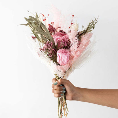 Hand holding a pastel pink rose dried bouquet mixed with green eucalyptus leaves and pampas grass for bohemian gifting.