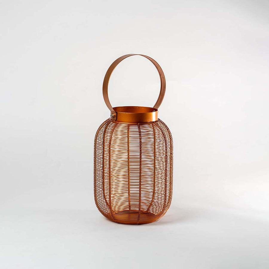 Copper metal mesh cylindrical lantern with circular carrying handle and ribbed texture design on isolated white background.