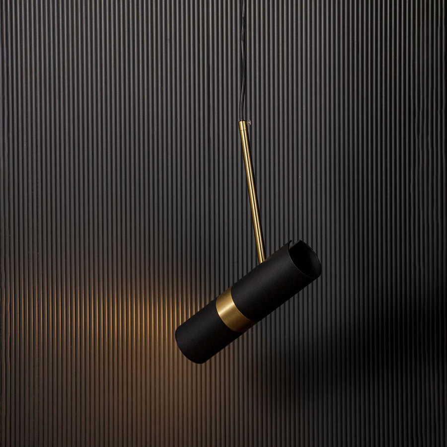 Modern black and gold cylindrical pendant lamp glowing warm light elegant ceiling fixture for bedroom and luxury home styling.