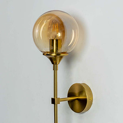 Closeup view of gold wall light focusing on the amber glass shade and warm inner bulb with fine detailing of the metal frame and finish.