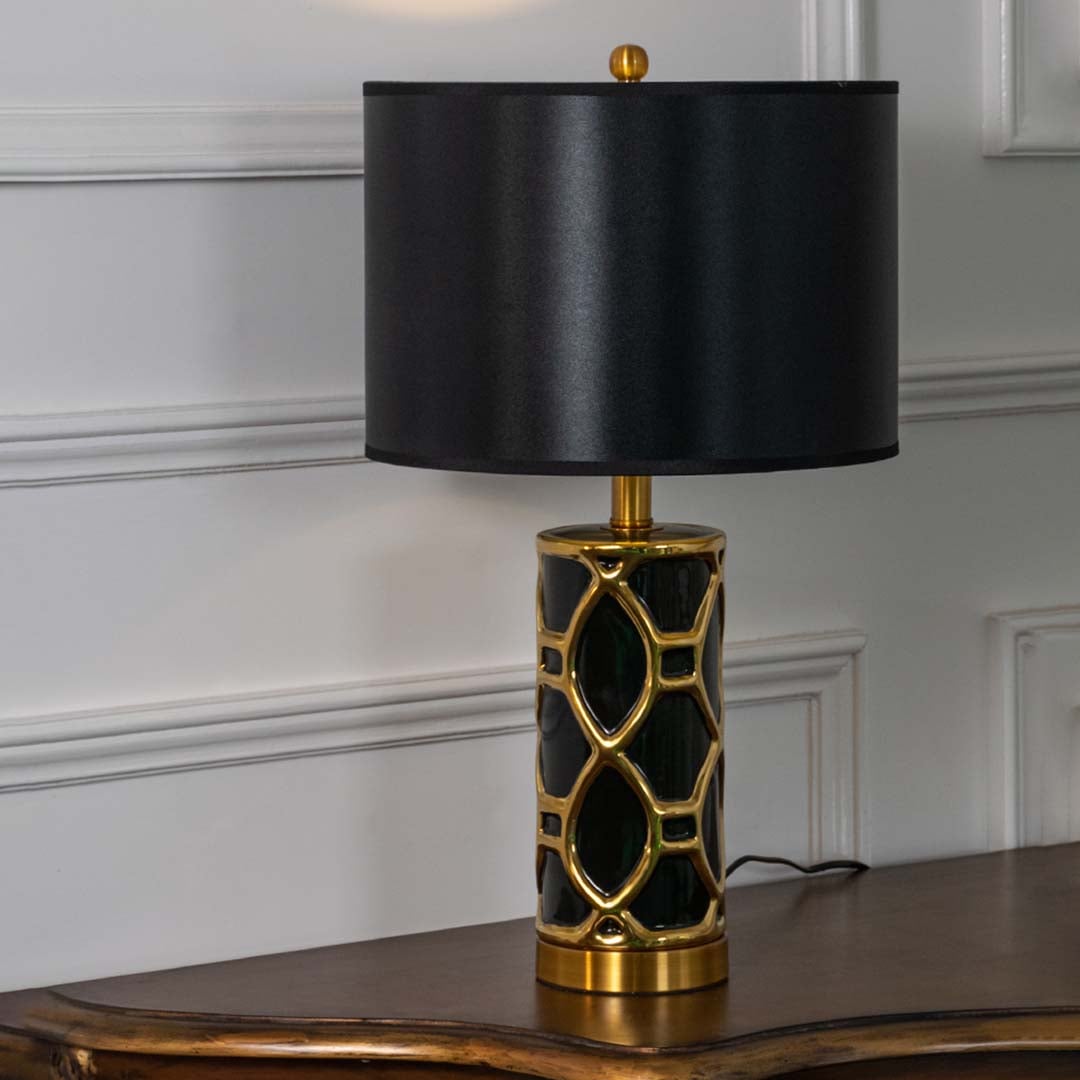Black and gold ceramic table lamp with black shade glowing softly on white background for luxurious home lighting.