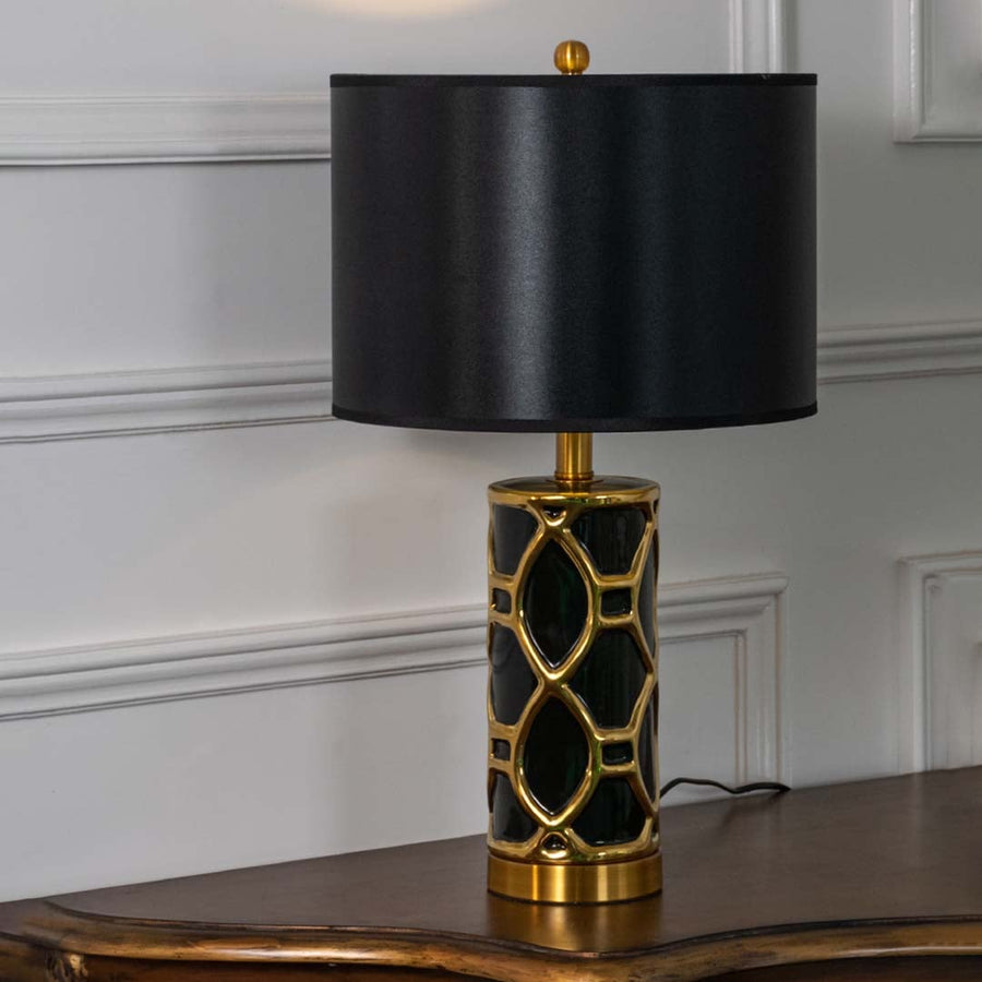 Black and gold ceramic table lamp with black shade glowing softly on white background for luxurious home lighting.
